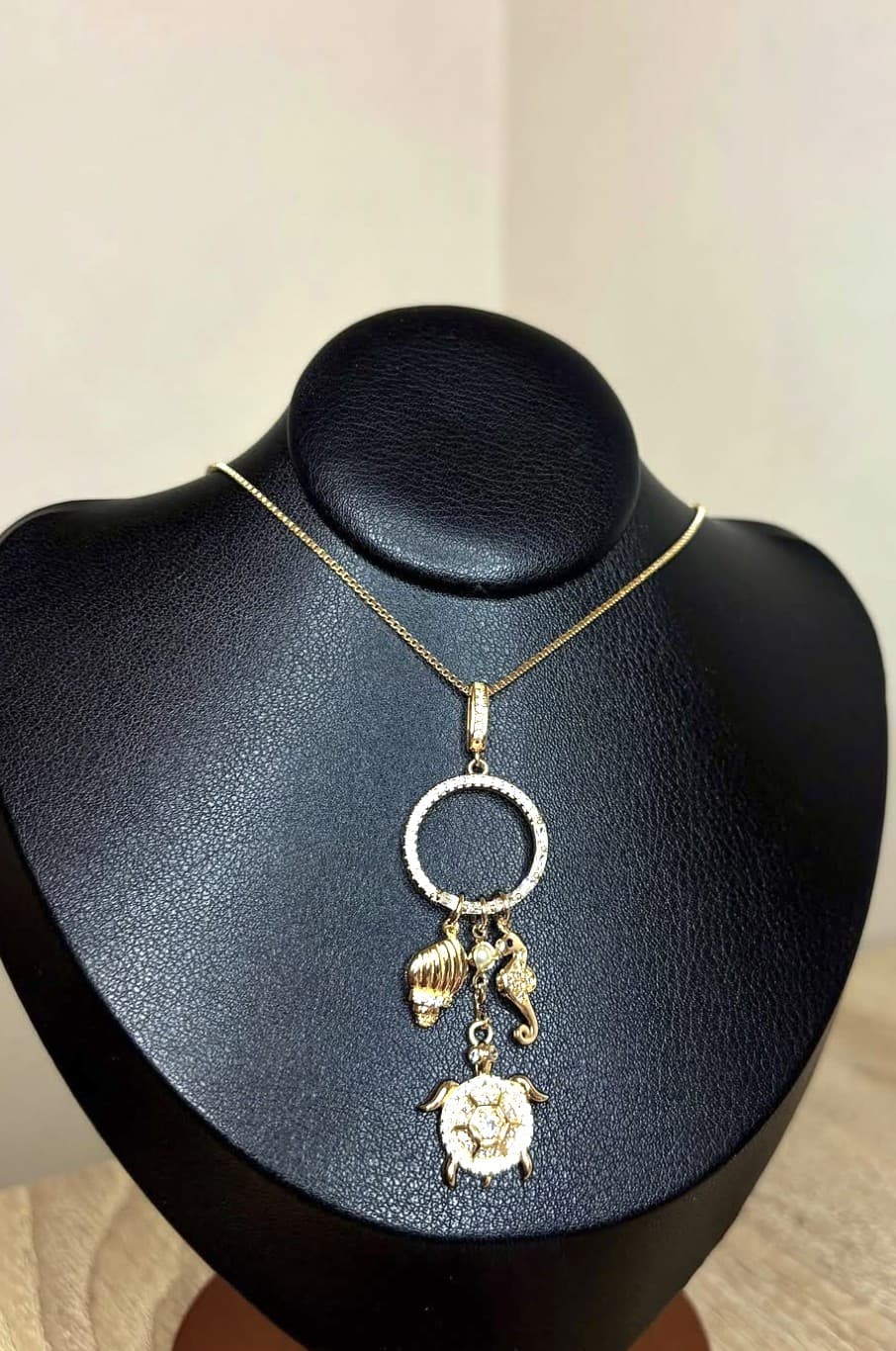 Collana dorata con cerchio e charms marini su busto espositore nero