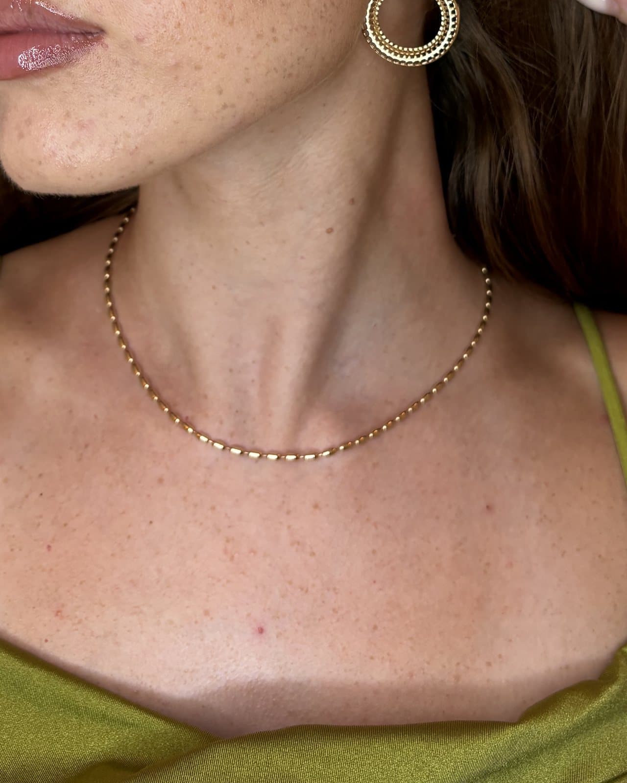 Collana dorata a maglia di piccoli grani, indossata