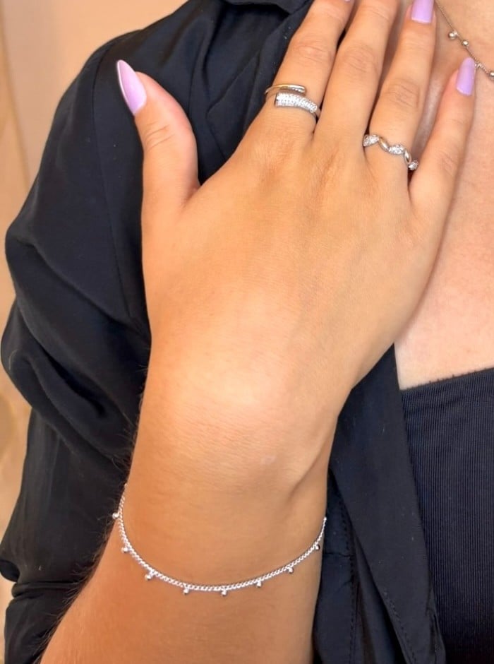 Mano appoggiata sul petto con anelli e bracciale a sfere in tono argento
