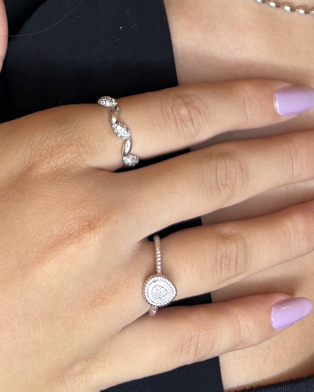 Mano con anello a goccia e anello ondulato in tono argento