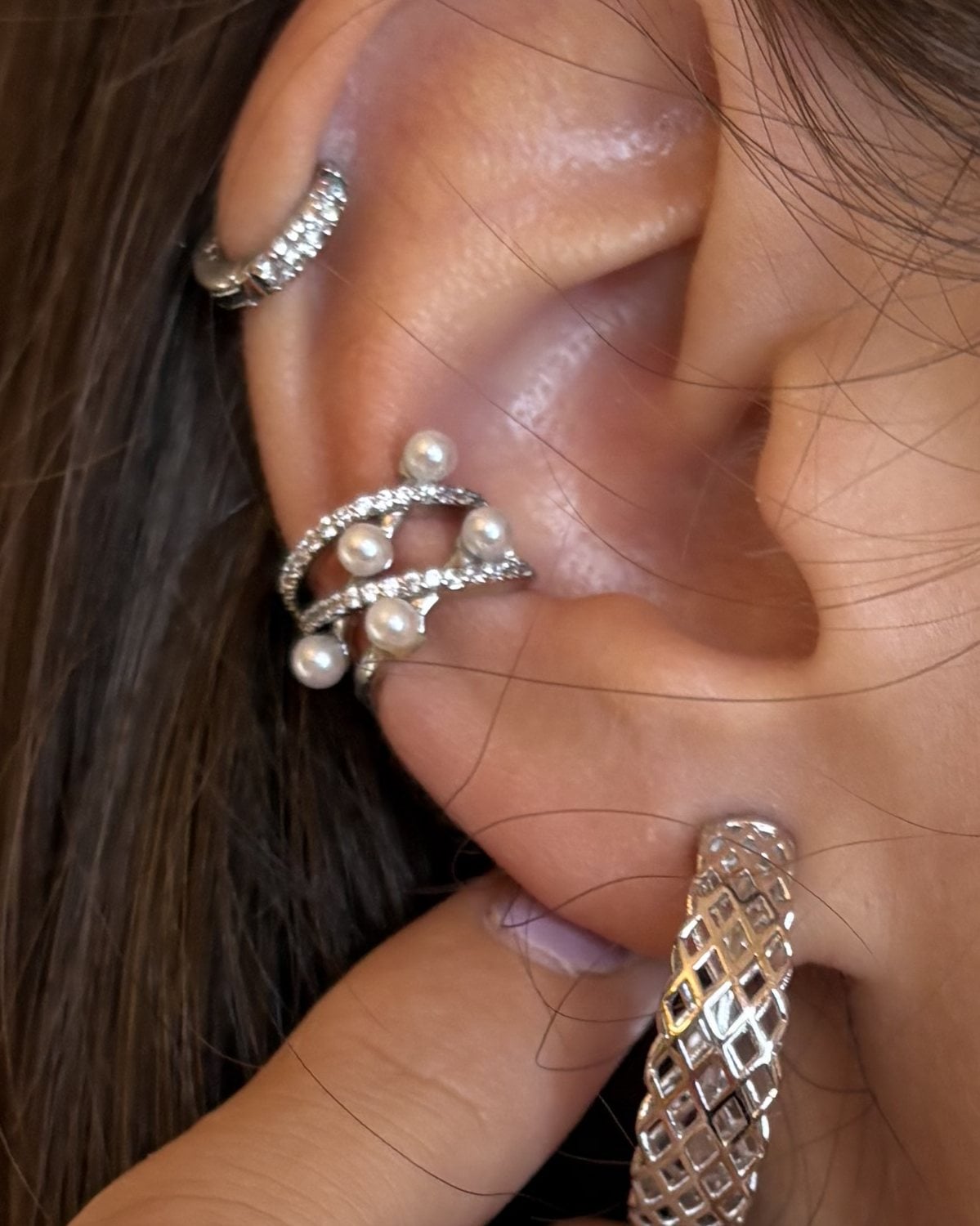 Ear cuff in tono argento con perline e zirconi, indossato; in alto un ear cuff sottile
